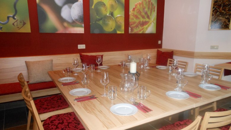 Ein Verkostungsraum mit gedecktem Holztisch, Weingl&auml;sern und Wandbildern von Weintrauben.