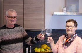 Zwei Personen stoßen mit Weingläsern in einer Küche an.