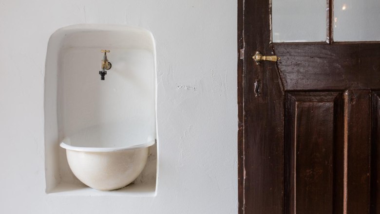 Ein alter Wasserhahn &uuml;ber einem eingelassenen Becken neben einer Holzt&uuml;r.